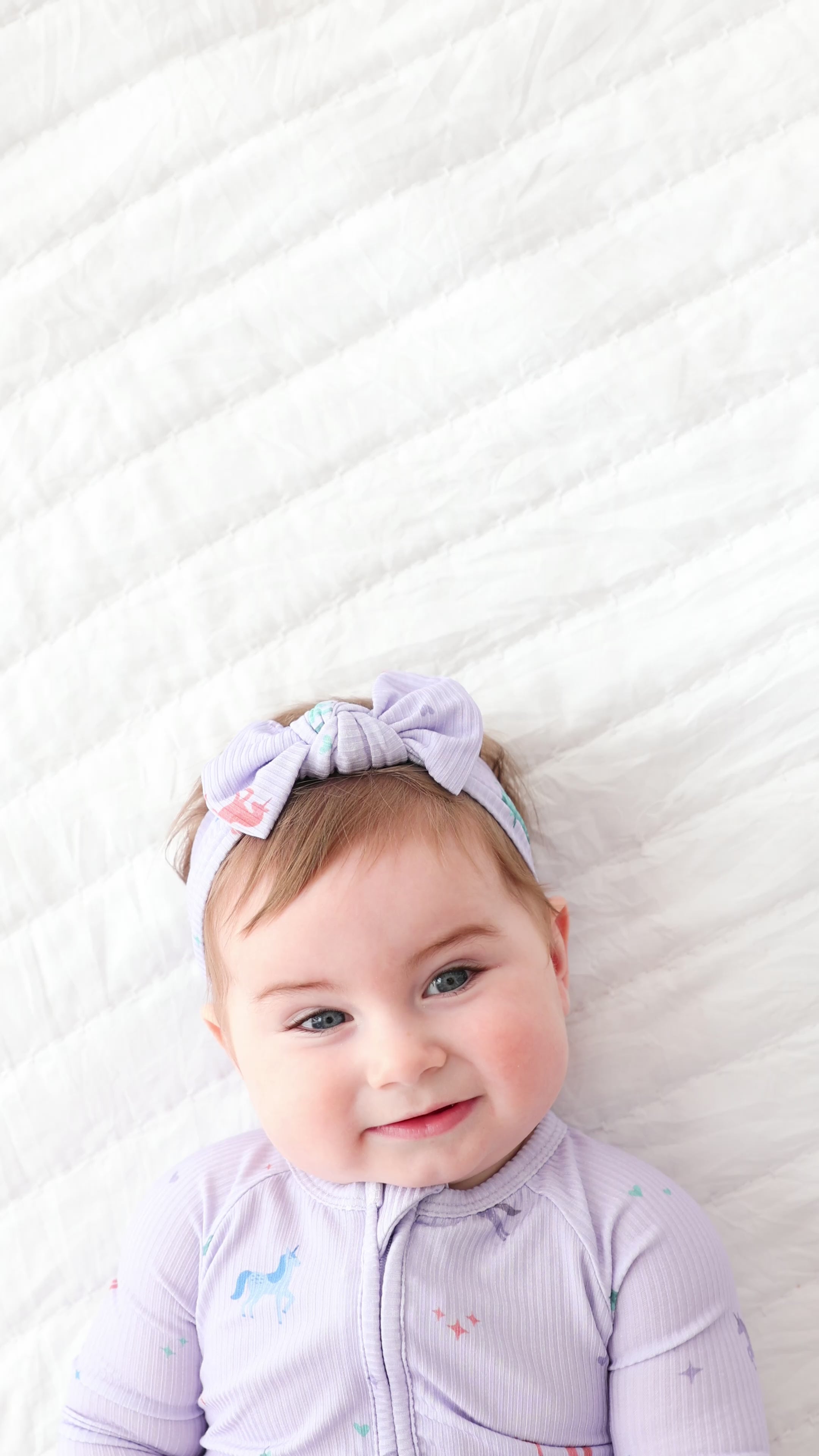 Video of a baby wearing a light purple outfit with horse designs and a matching headband on a white background