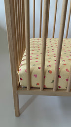 Wooden crib on a yellow fitted sheet with fruits and girly elements