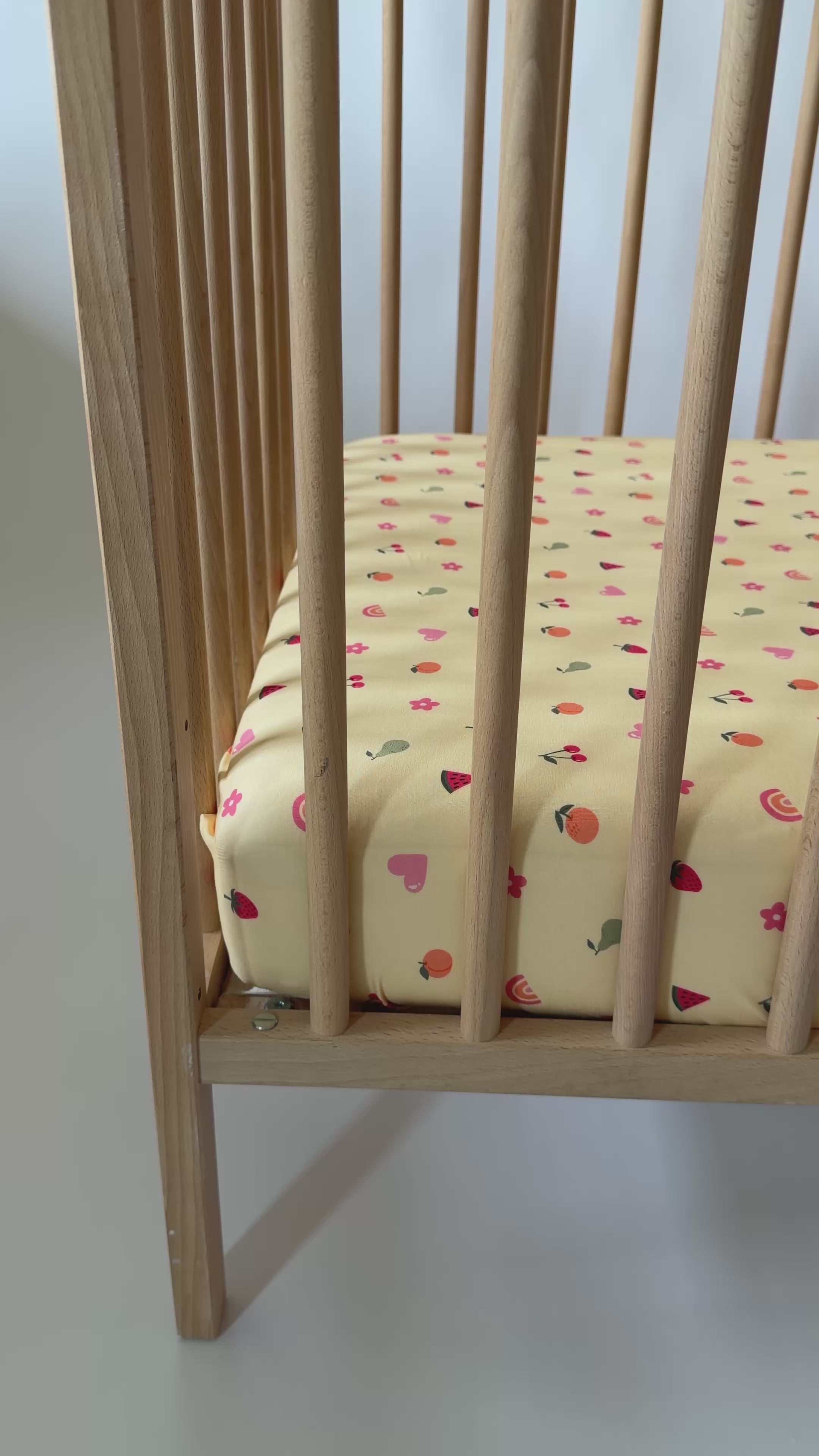 Wooden crib on a yellow fitted sheet with fruits and girly elements