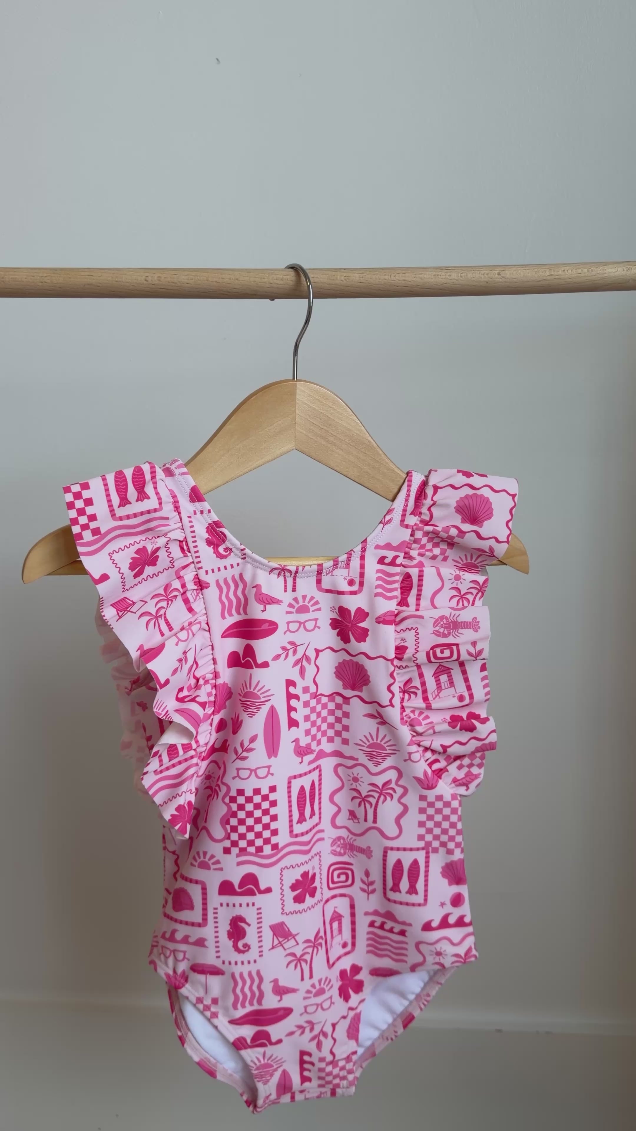 Pink and white patterned ruffled one-piece swimsuit hanging on a rack