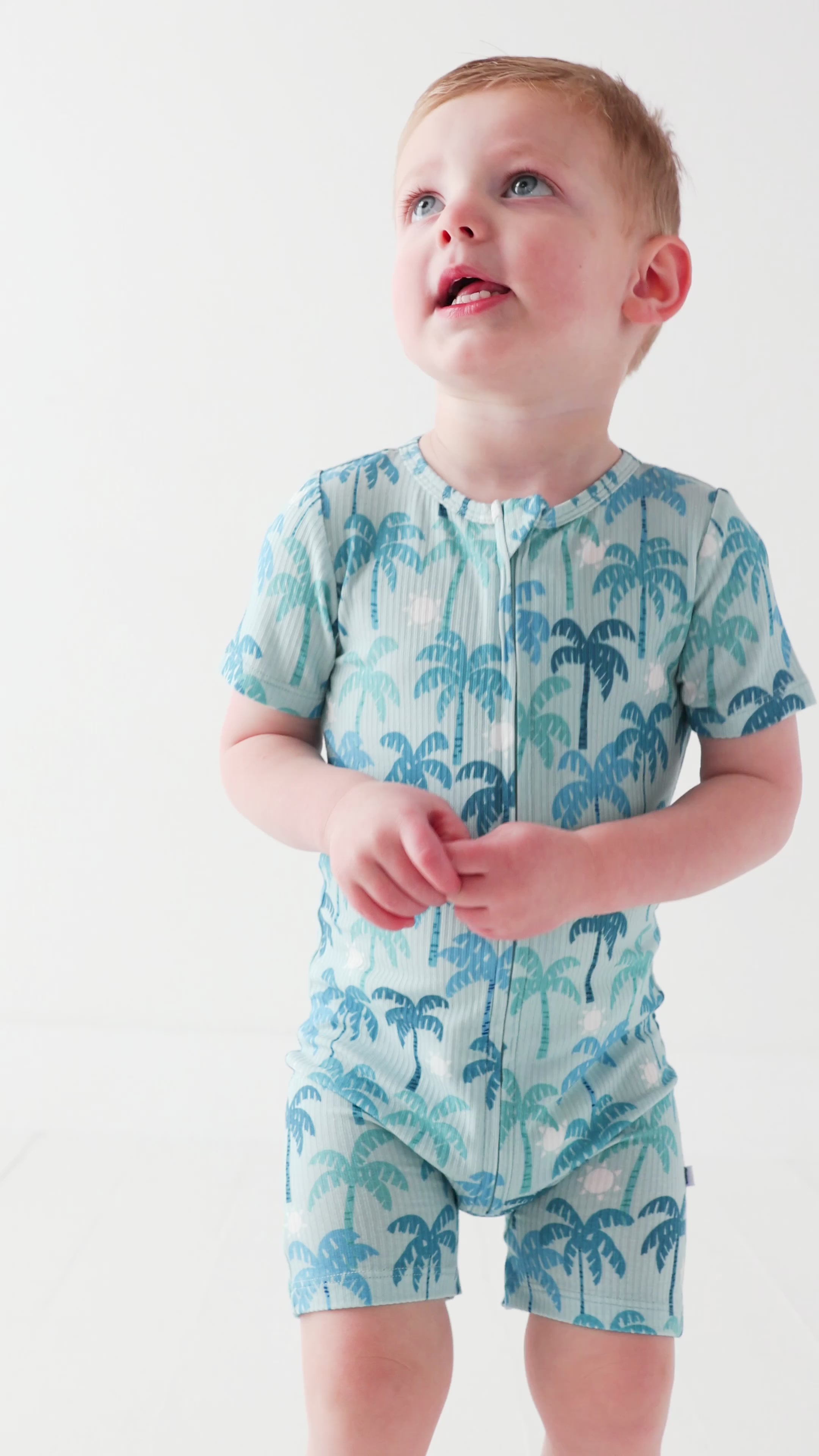 Child wearing a blue palm tree patterned onesie on a white background