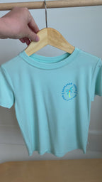 Light blue t-shirt with a palm tree design hanging on a rack