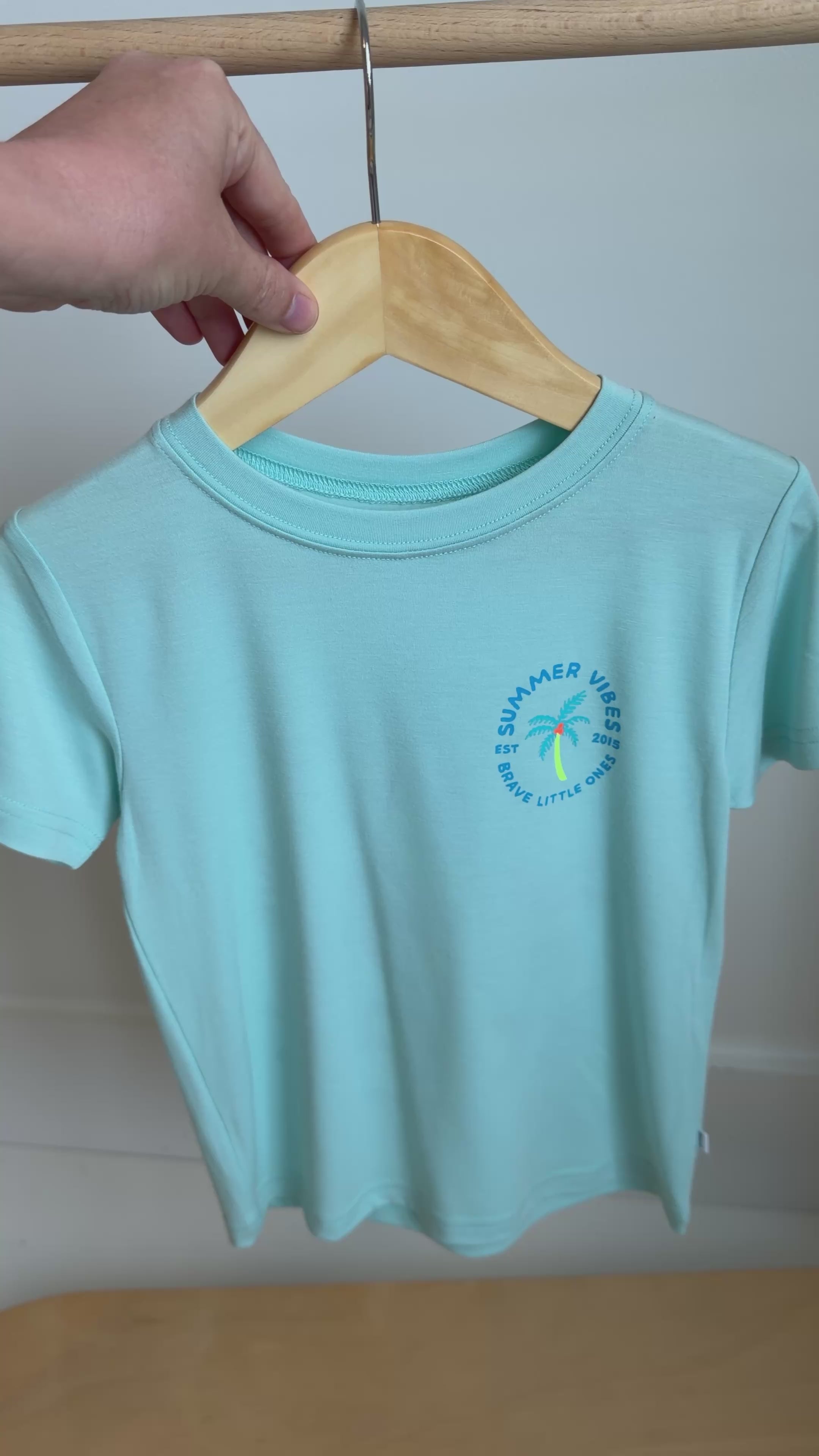 Light blue t-shirt with a palm tree design hanging on a rack
