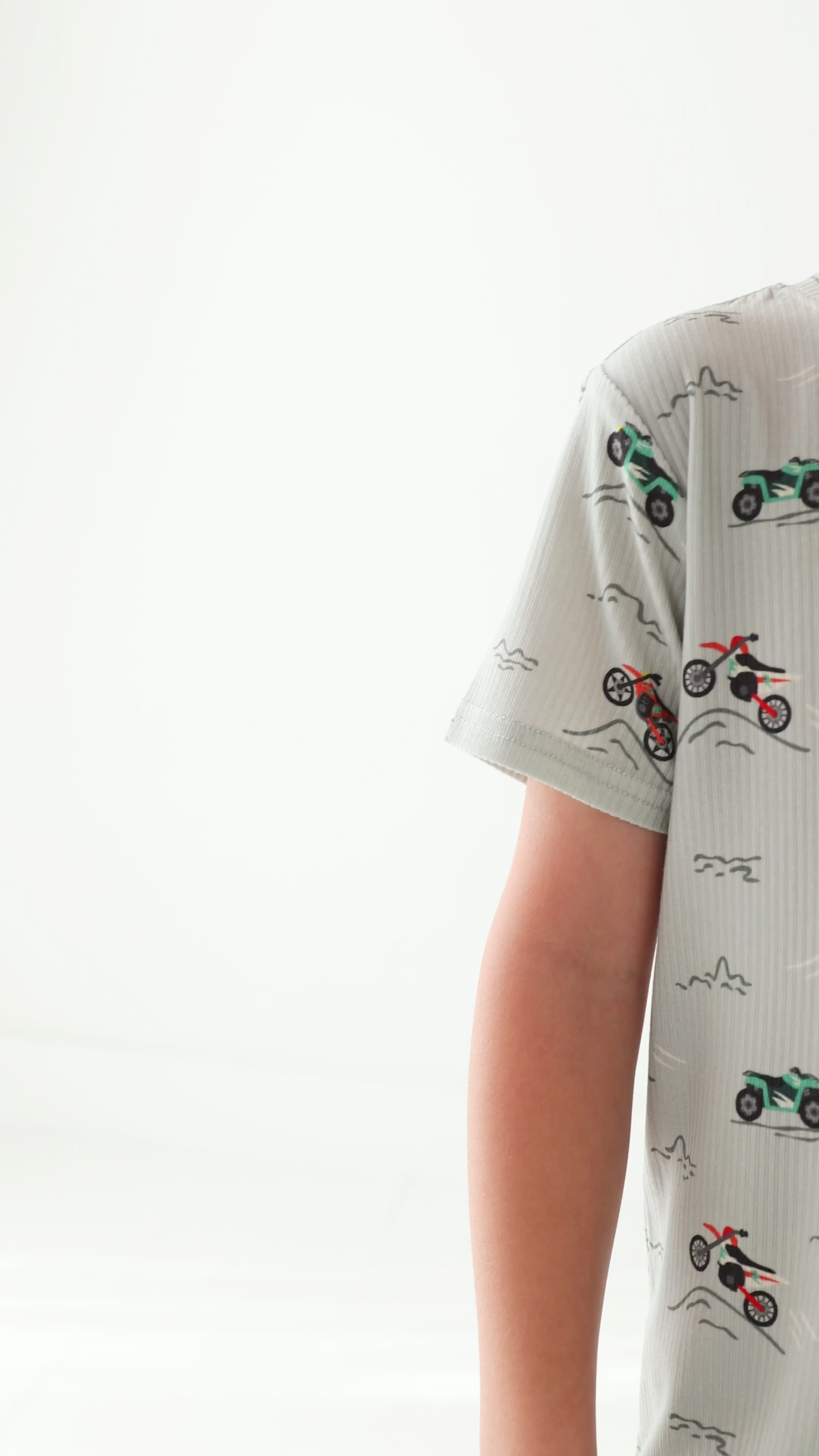 Child wearing a light gray short pajama set with vehicle pattern on a white background