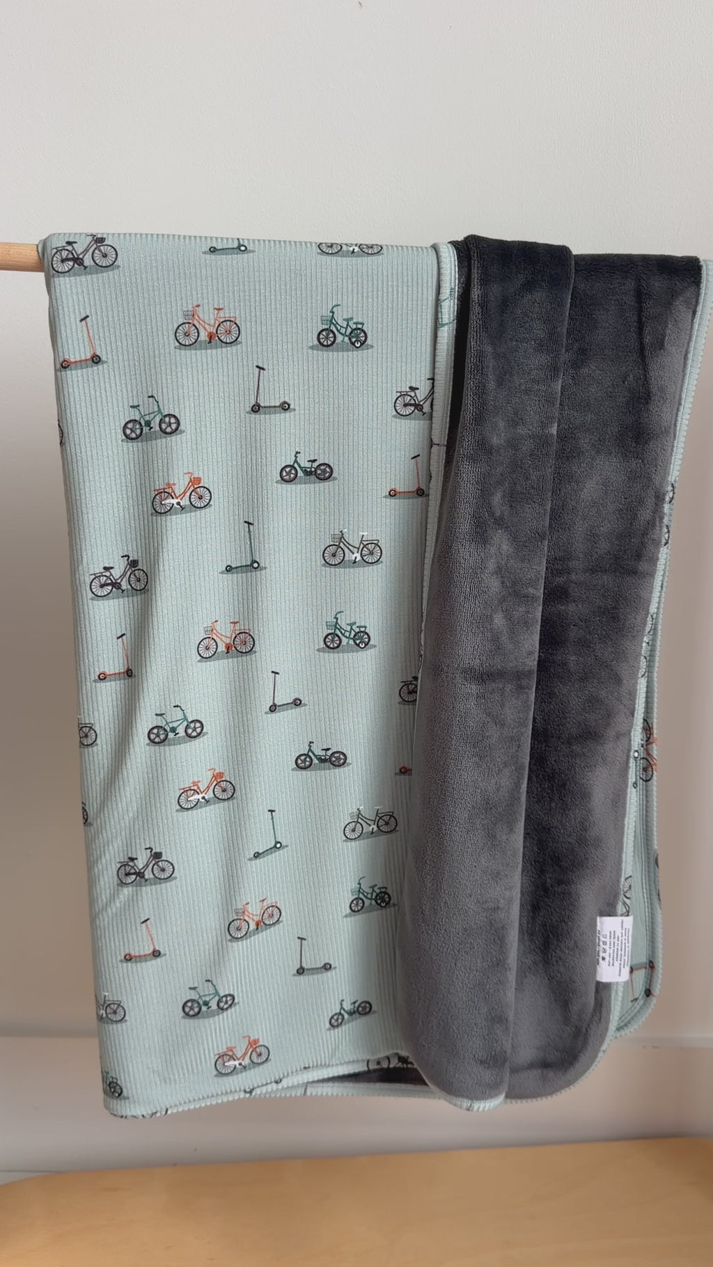 Video of a children's blanket with bicyles & scooters pattern draped on a hanging rack