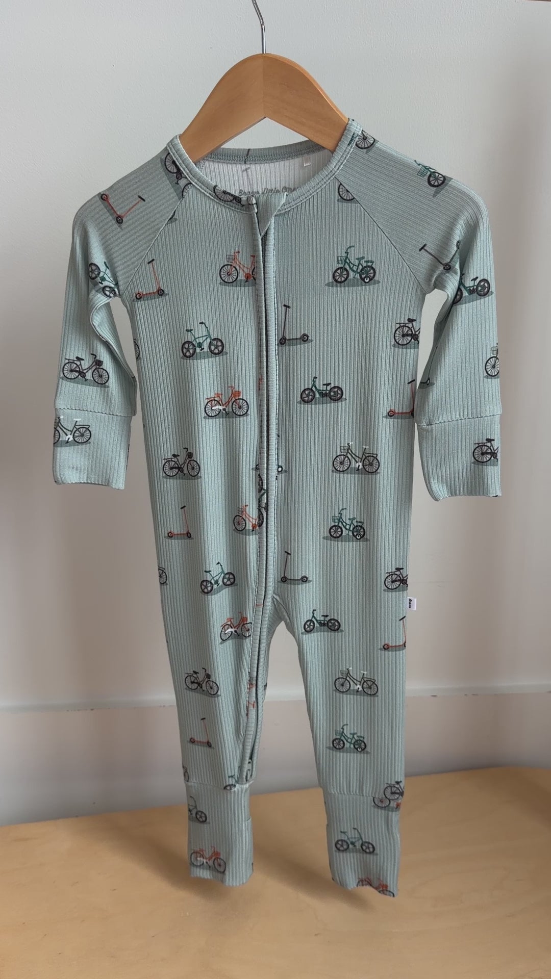 Video of a children's onesie with bicycles & scooters pattern hanging on a rack