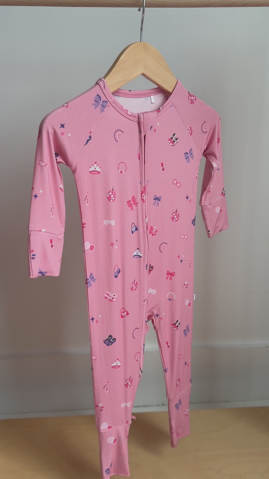 Video of a pink baby onesie with girly patterns hanging on a rack