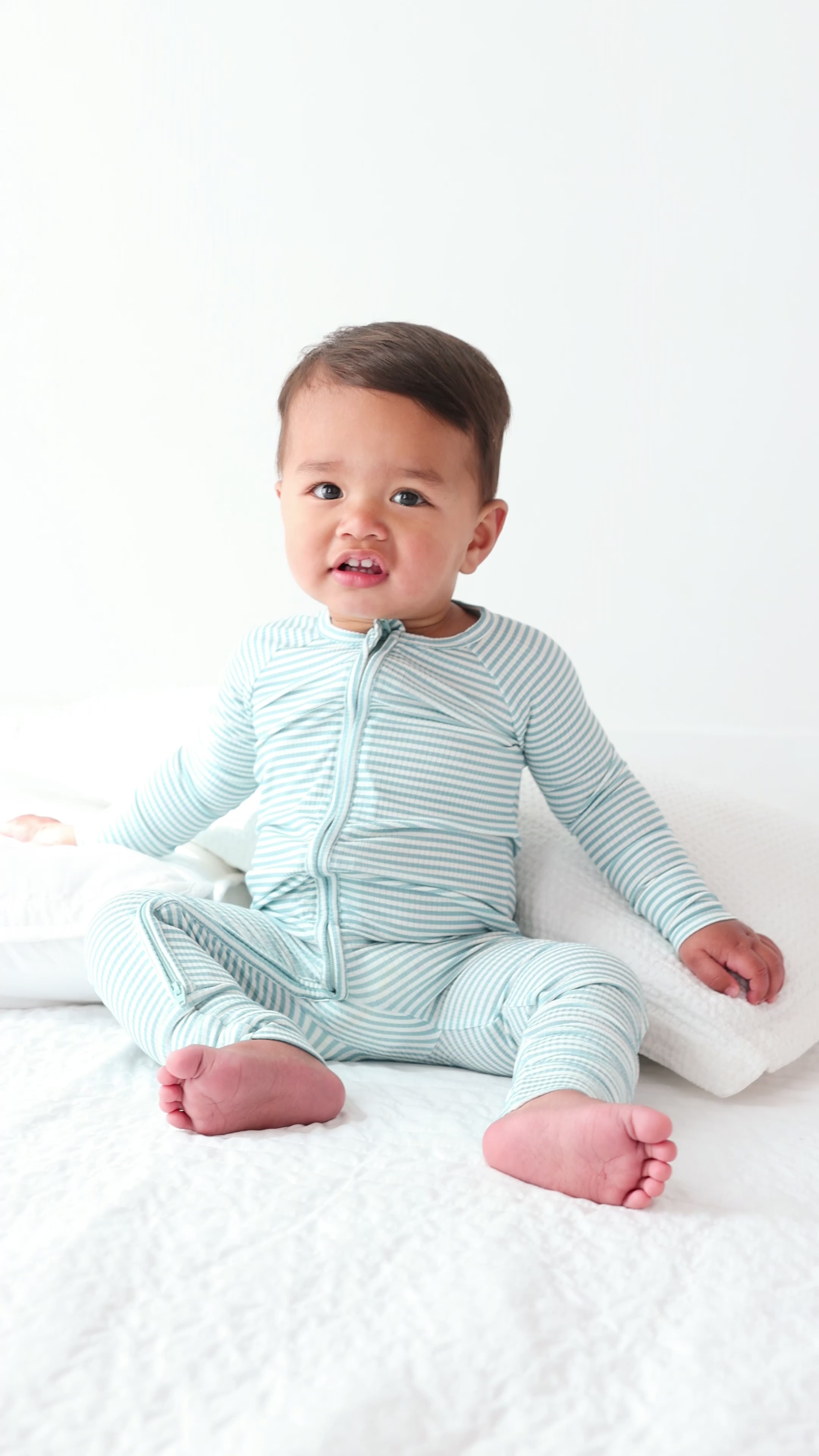Video of a baby wearing a light blue and white striped onesie on a plain background