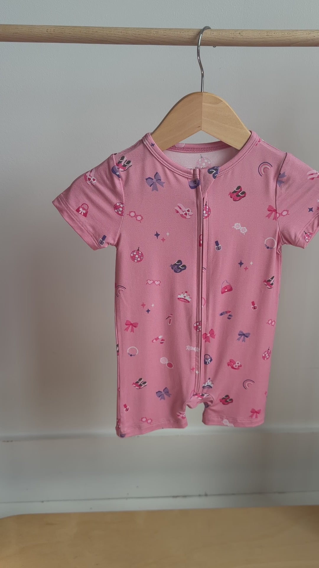 Video of a pink baby romper with colorful girly patterns hanging on a rack