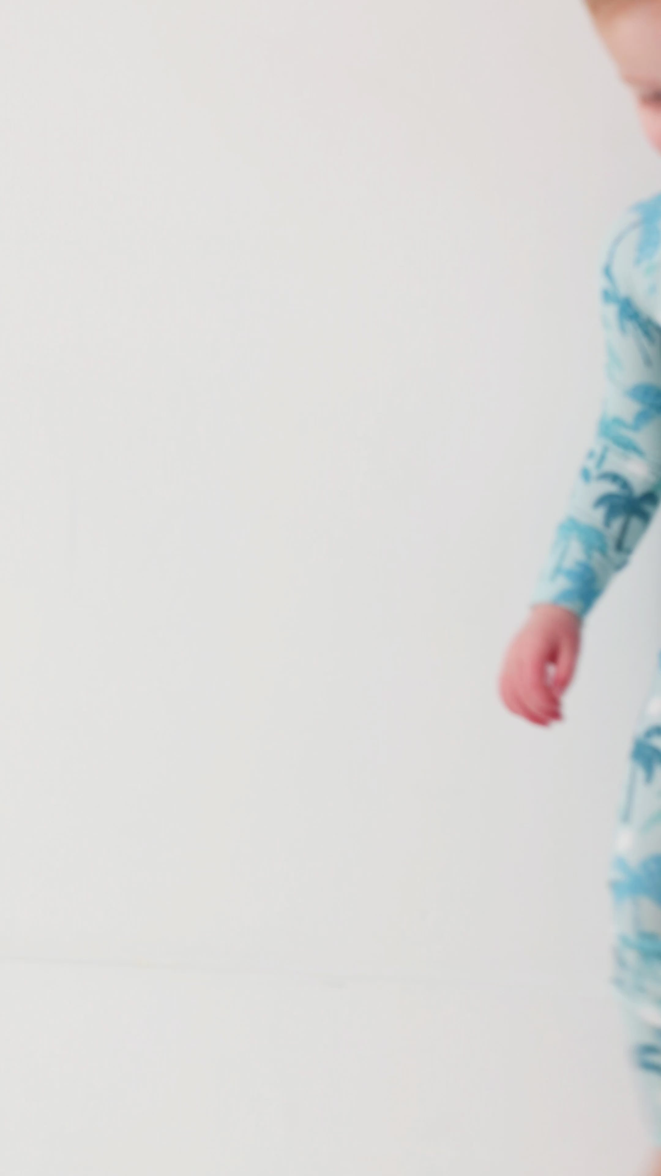 Child wearing a blue palm tree patterned onesie on a white background