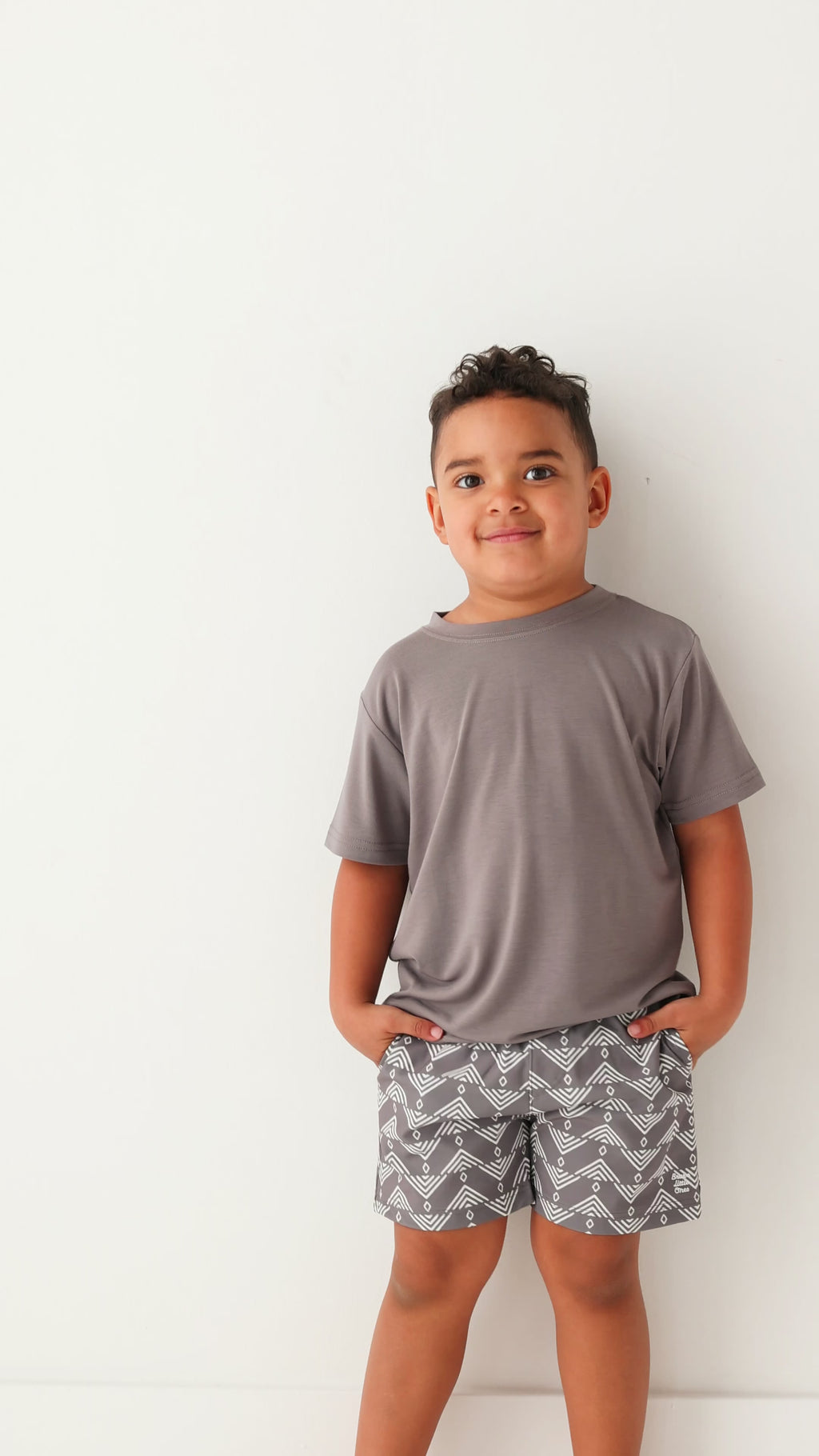 Child wearing a gray t-shirt and geometric-patterned shorts on a white background