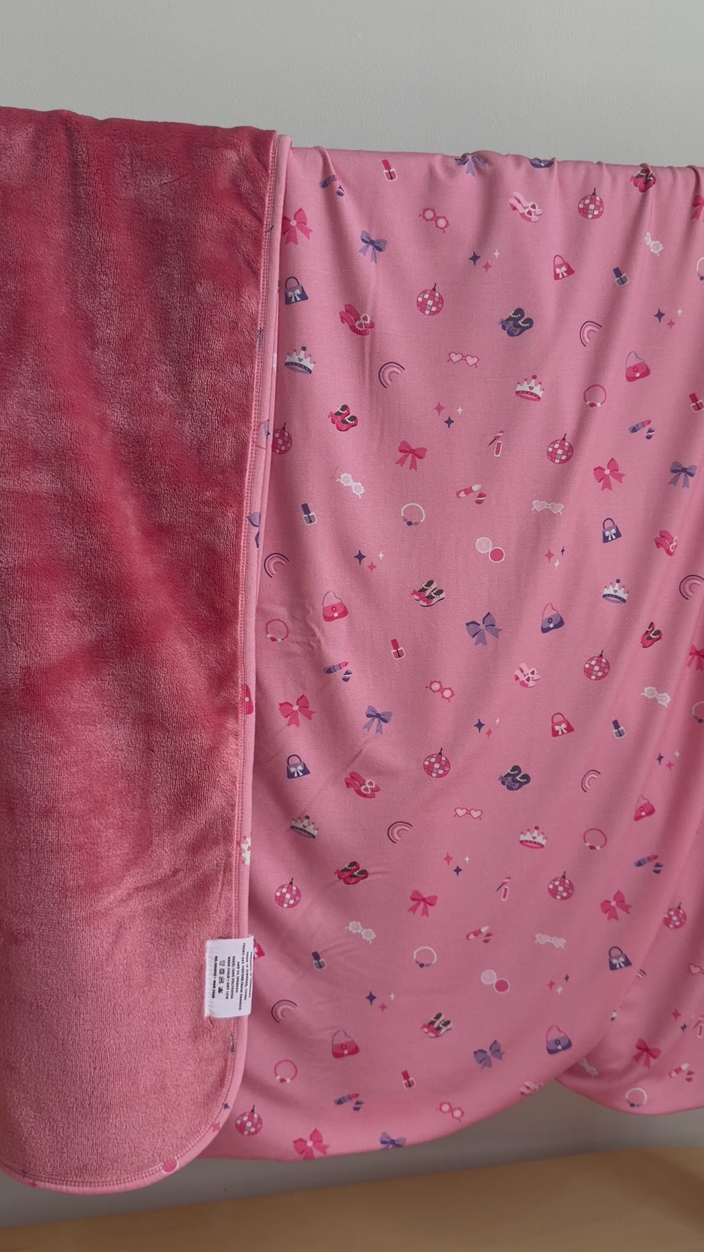 Pink blanket with small girly patterns draped over a hanging rack