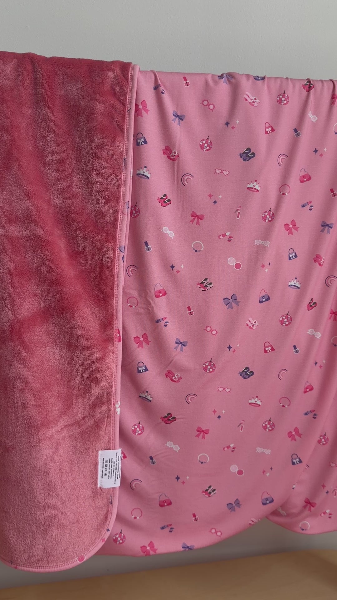 Pink blanket with small girly patterns draped over a hanging rack