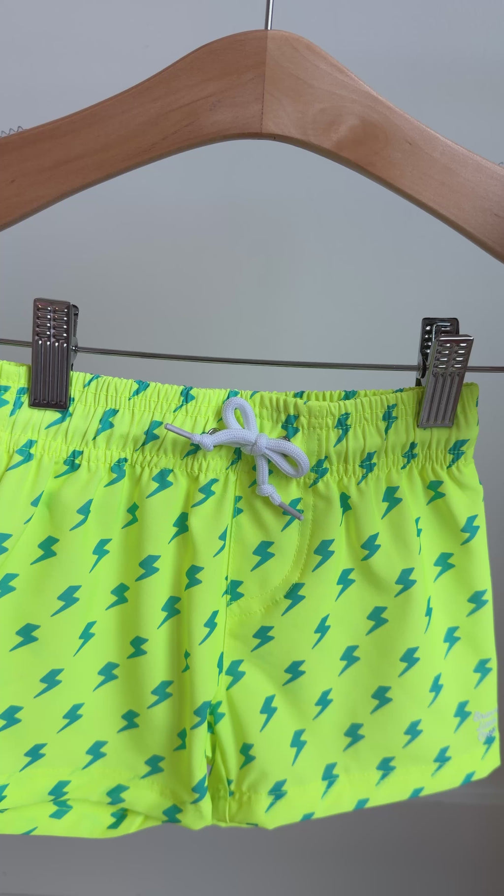 Neon yellow swim shorts with blue lightning bolt pattern hanging on a rack