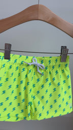 Neon yellow swim shorts with blue lightning bolt pattern hanging on a rack