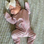 Newborn baby in a pink and white striped outfit with a large bow on a textured surface
