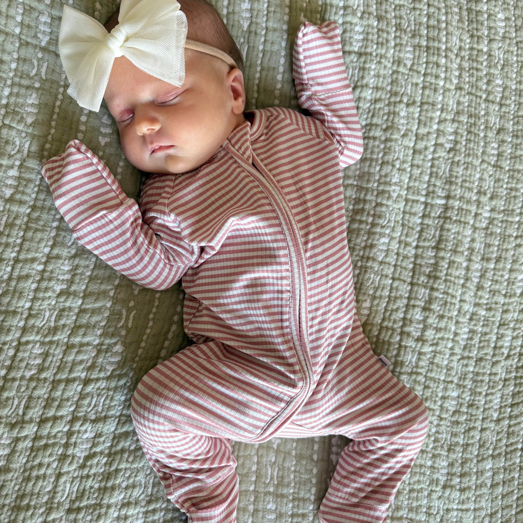 Newborn baby in a pink and white striped outfit with a large bow on a textured surface
