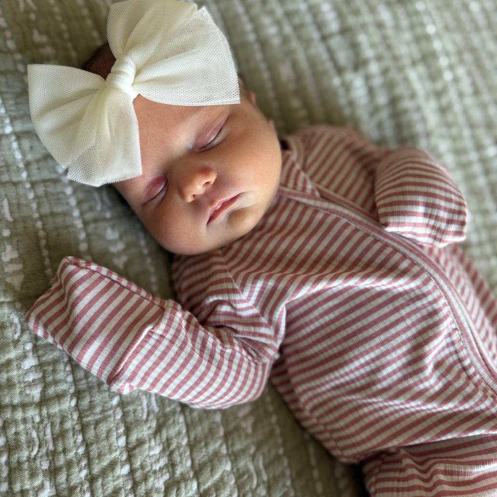Newborn baby in a pink and white striped outfit with a large bow on a textured surface