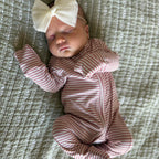 Newborn baby in a pink and white striped outfit with a large bow on a textured surface