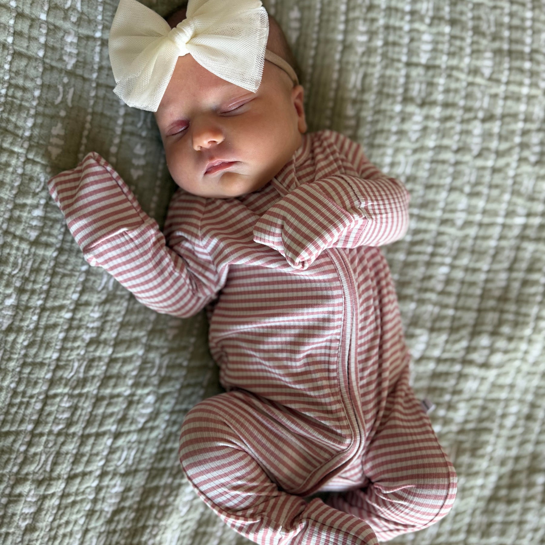 Newborn baby in a pink and white striped outfit with a large bow on a textured surface