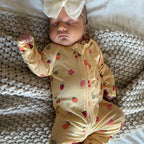 Newborn baby in a yellow outfit with fruit patterns, lying on a textured blanket.